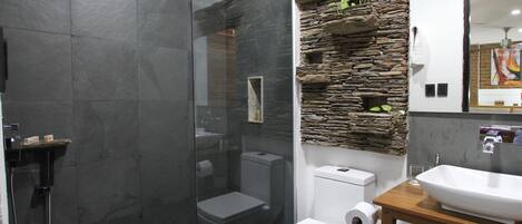 Un baño moderno con ducha de vidrio, inodoro blanco y tocador de madera con lavamanos blanco.