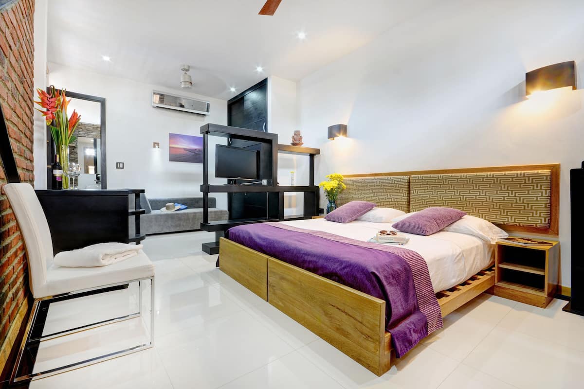 A modern bedroom with a wooden bed, a TV, a chair, and a desk.