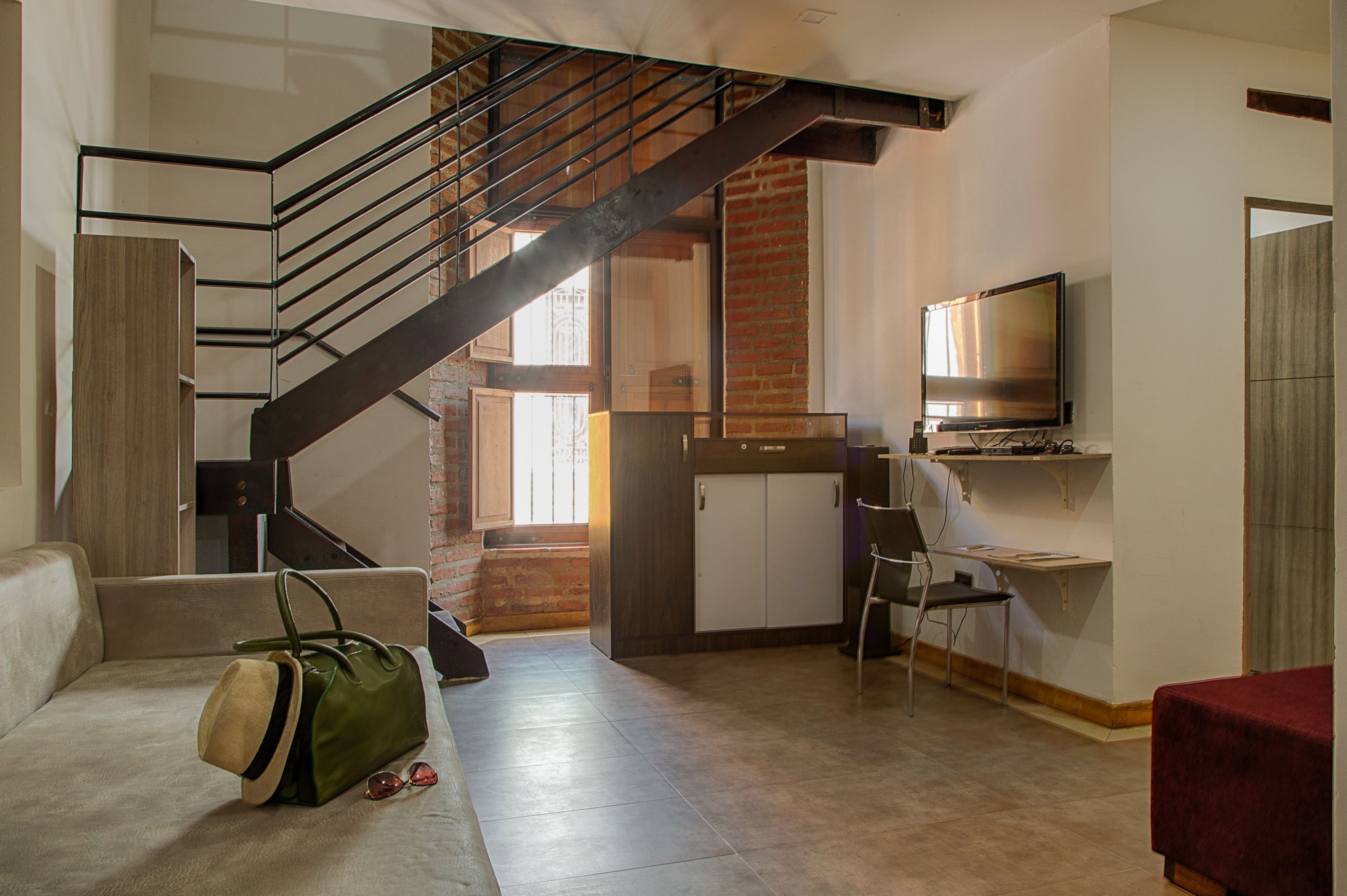 Un espacio habitable moderno con una escalera, un televisor, un escritorio y un sofá rojo.
