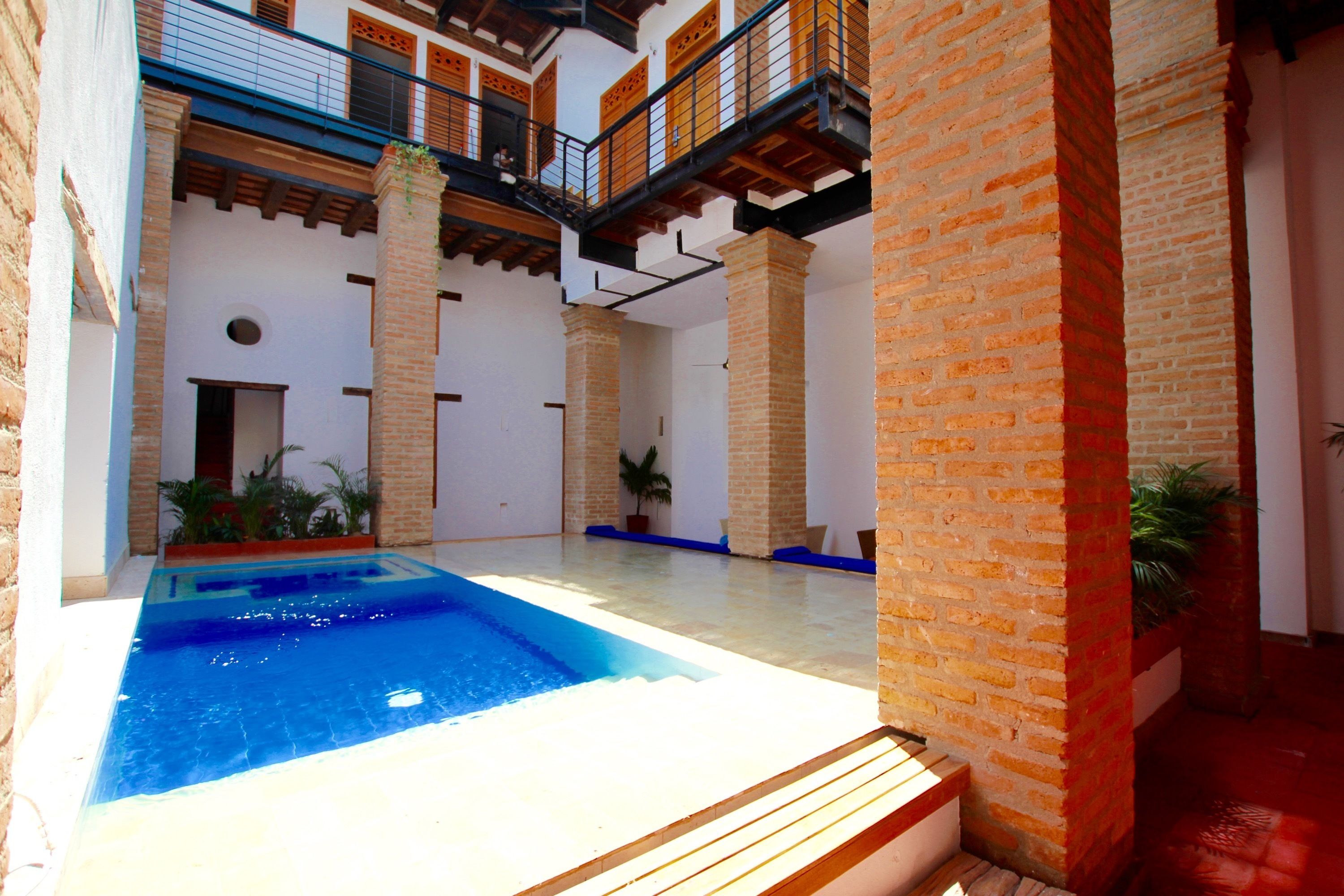 A swimming pool with a wooden deck, surrounded by brick pillars and potted plants.