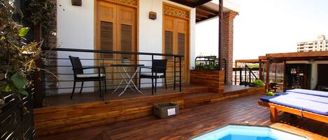 Una terraza de madera con piscina, dos puertas de madera y una mesa con sillas.