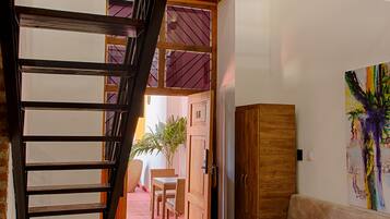 A staircase leading to a dining area with a table and chairs, a sofa, and a painting on the wall.