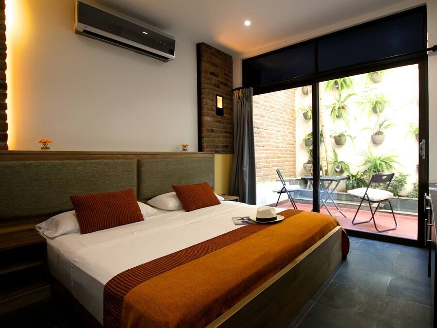 A hotel room with a large bed, a nightstand, a window with a view of the outside, and a small table with chairs.