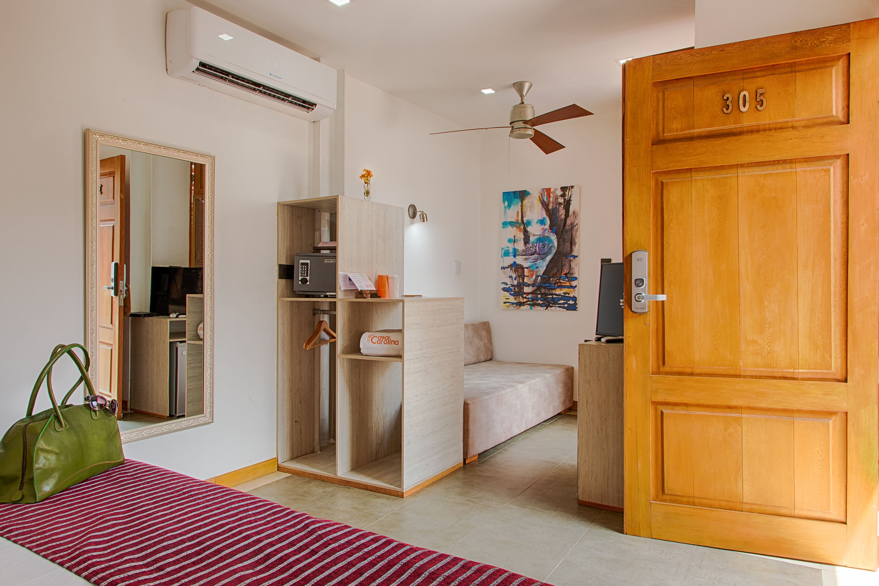 A hotel room with a bed, a wardrobe, a desk, and a door with the number 305.