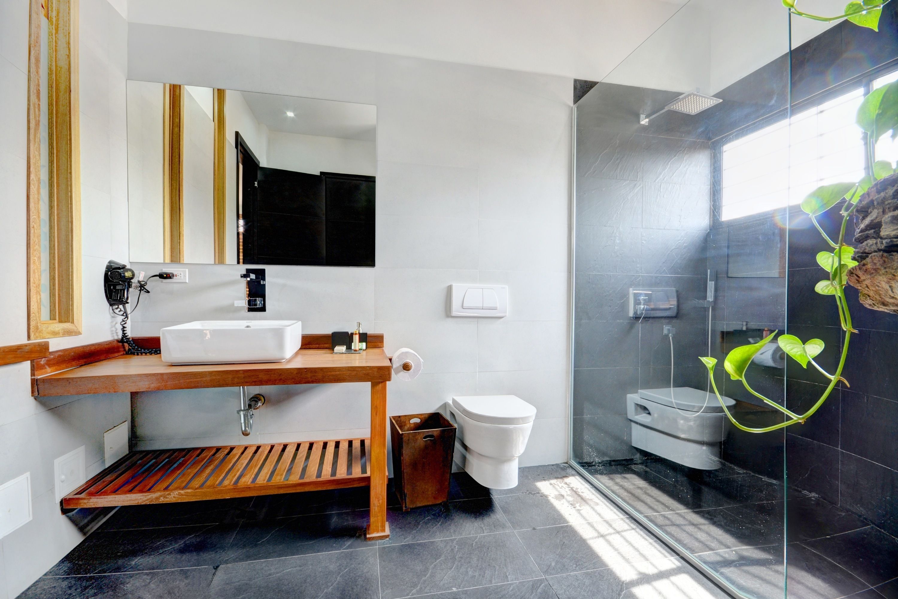 A modern bathroom with a wooden vanity, a large mirror, a white sink, a toilet, and a glass-enclosed shower area.