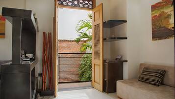 Un espacio habitable pequeño con kitchenette, un sofá, una puerta que da a un balcón y una mesita con un teléfono.