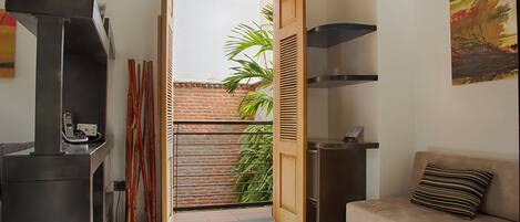 Un espacio habitable pequeño con kitchenette, un sofá, una puerta que da a un balcón y una mesita con un teléfono.