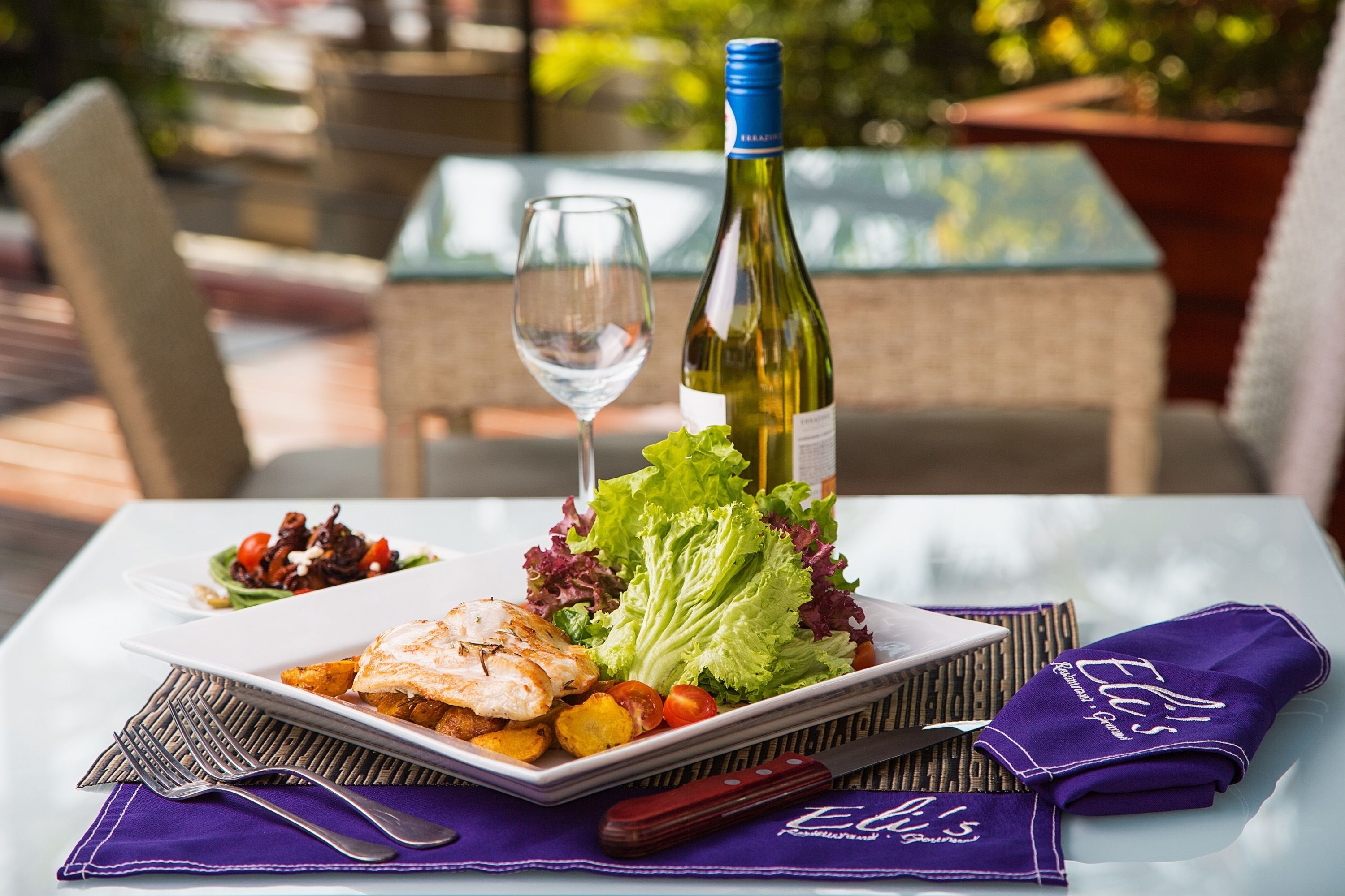 A table set with a plate of food, a wine bottle, and a glass of wine.