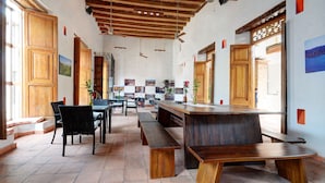 Una habitación amplia con techo de madera, ventanas grandes y una larga mesa de madera con bancos.