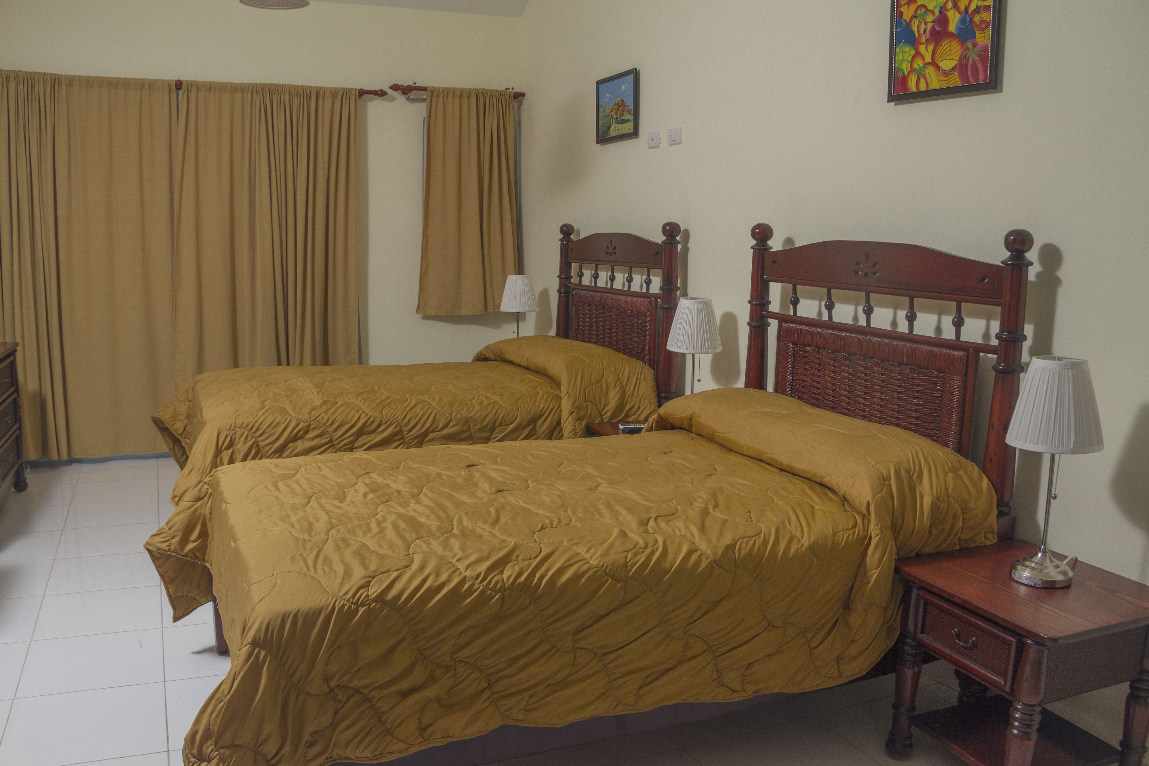 Una habitación con dos camas, una mesita de noche, una lámpara, un ventanal con cortinas y una pared decorada con un cuadro.