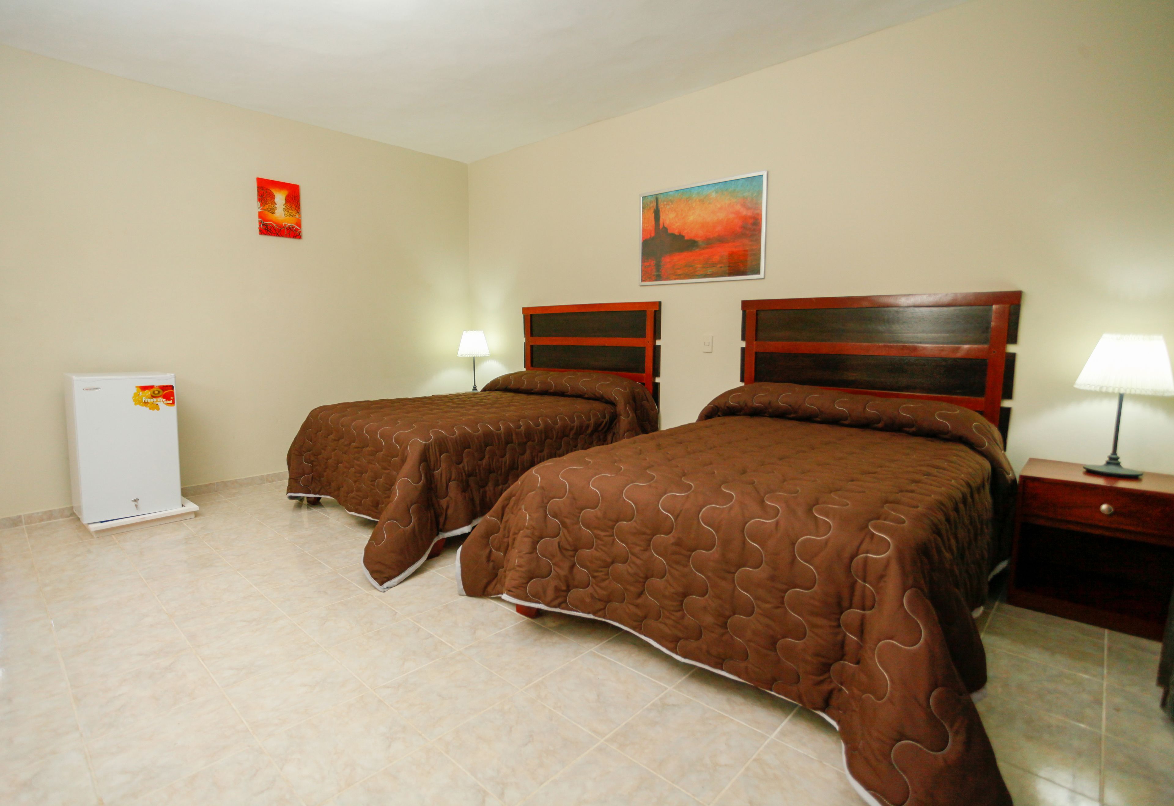 Habitación de hotel con dos camas, un refrigerador y una mesita de noche con lámpara.