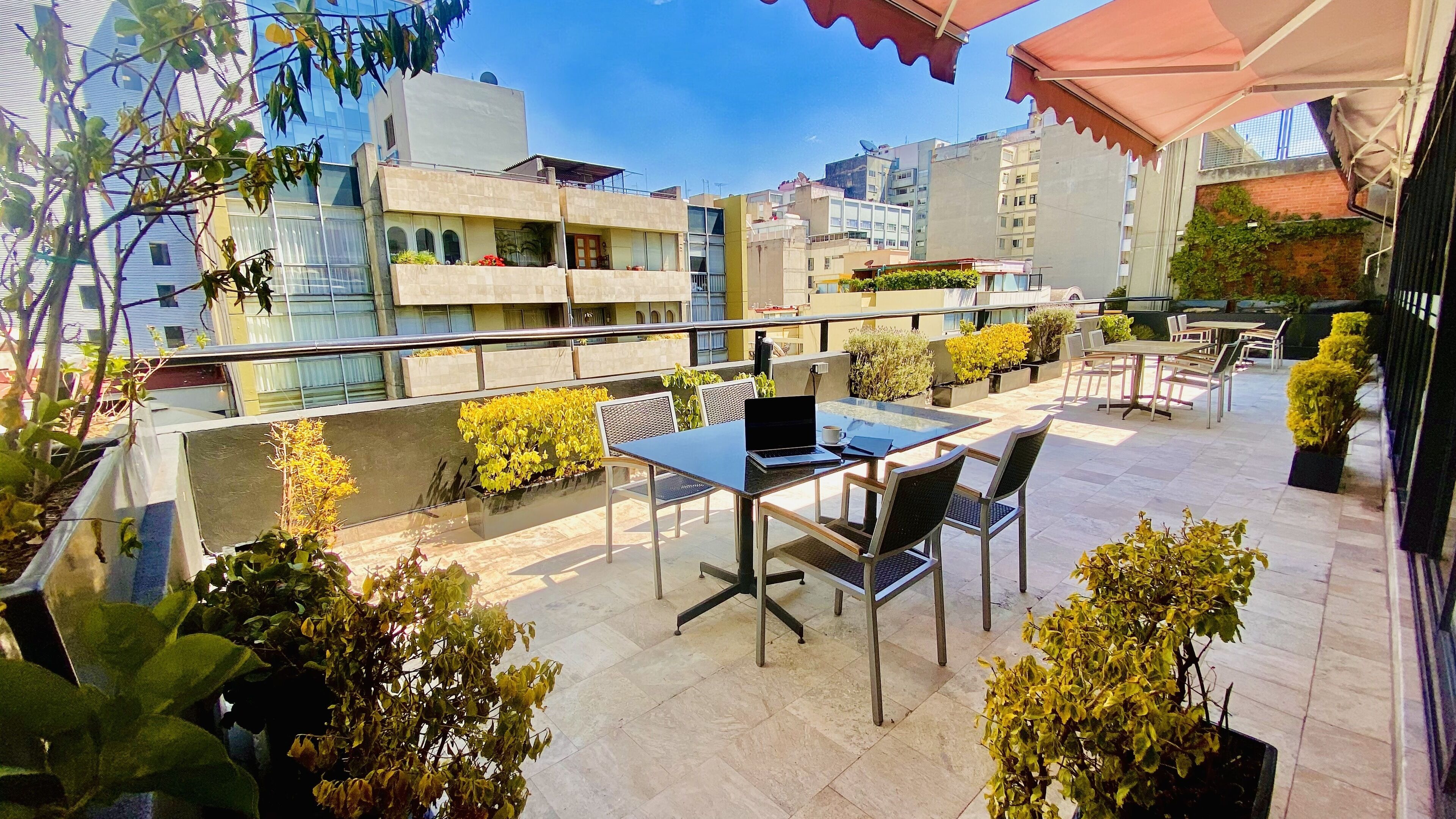 A rooftop terrace with a table, chairs, and a laptop.