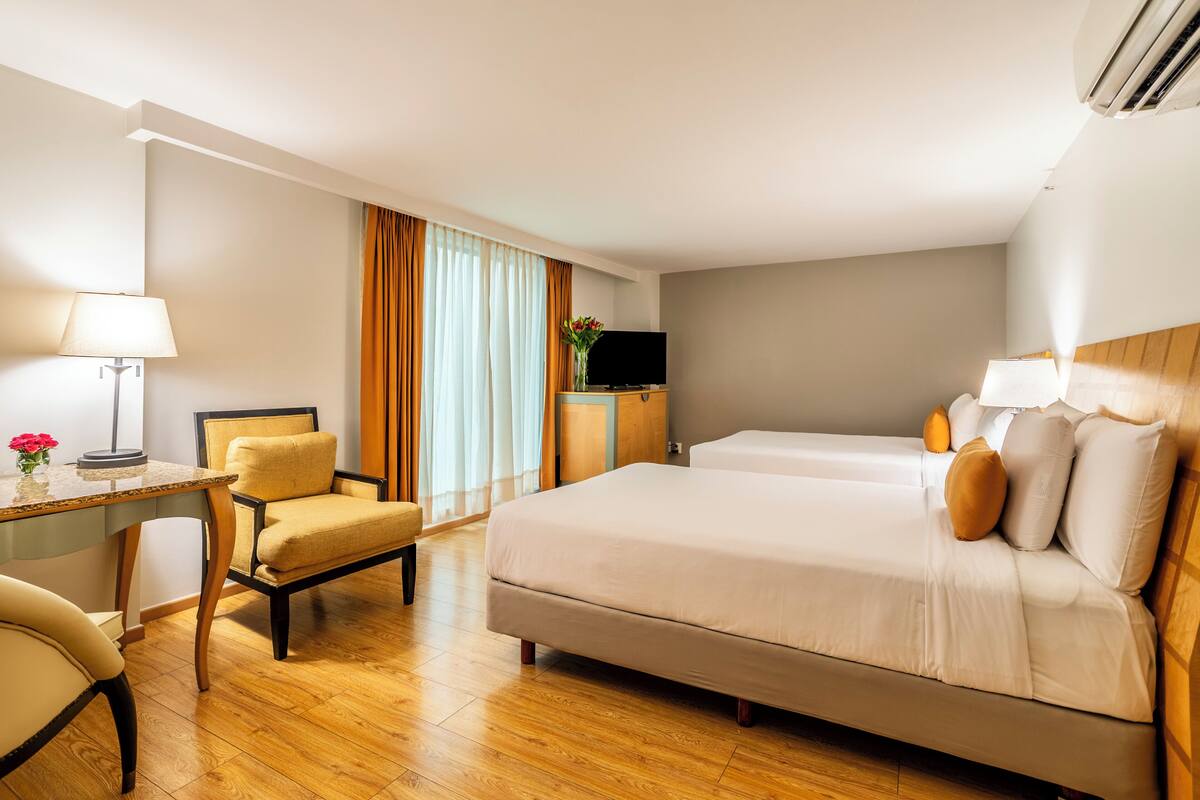 A hotel room with a bed, a desk, a chair, a TV, and a window with curtains.