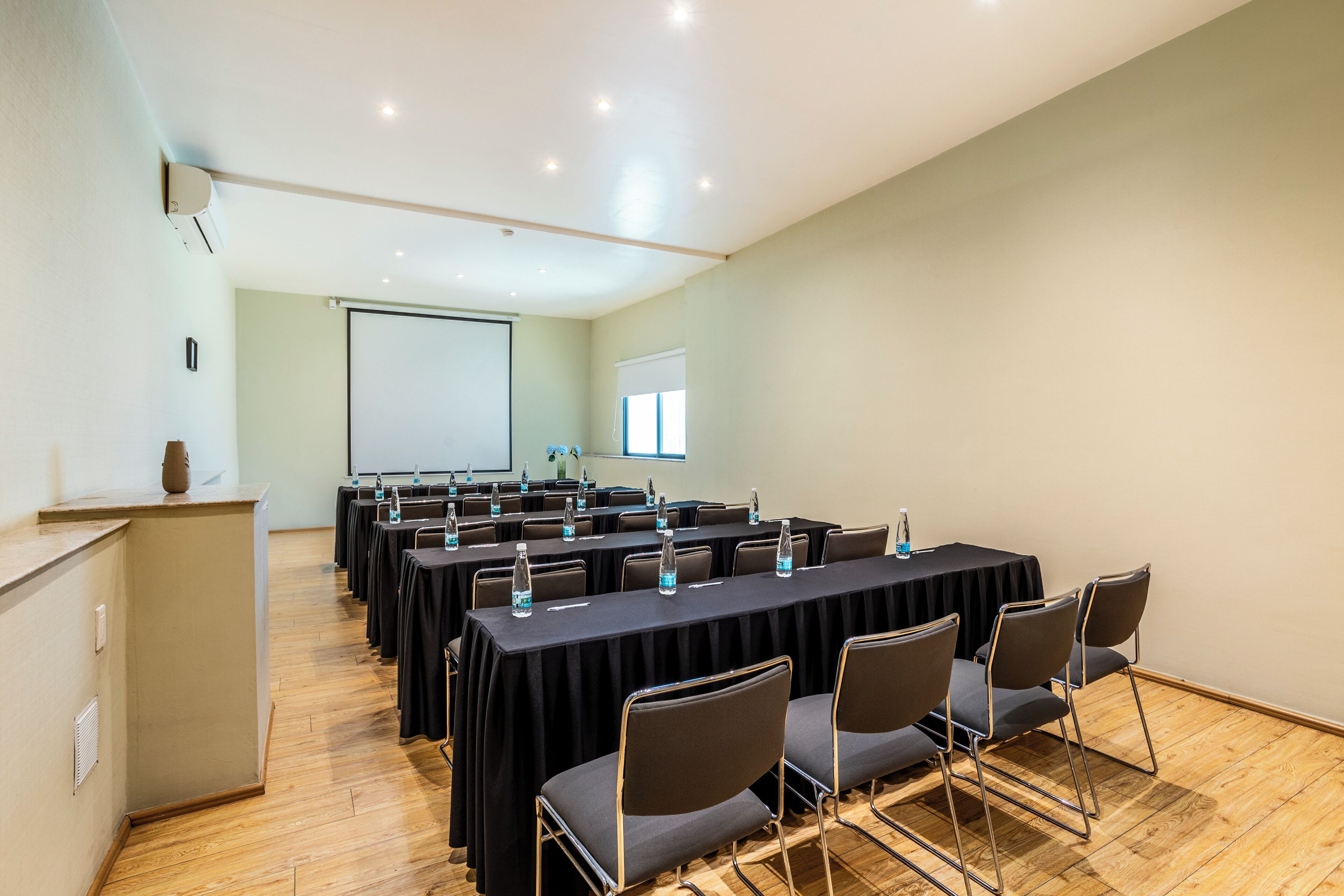 Un salón de conferencias con varias mesas, sillas y una pantalla para proyector.