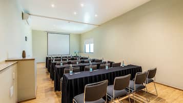 Un salón de conferencias con varias mesas, sillas y una pantalla para proyector.