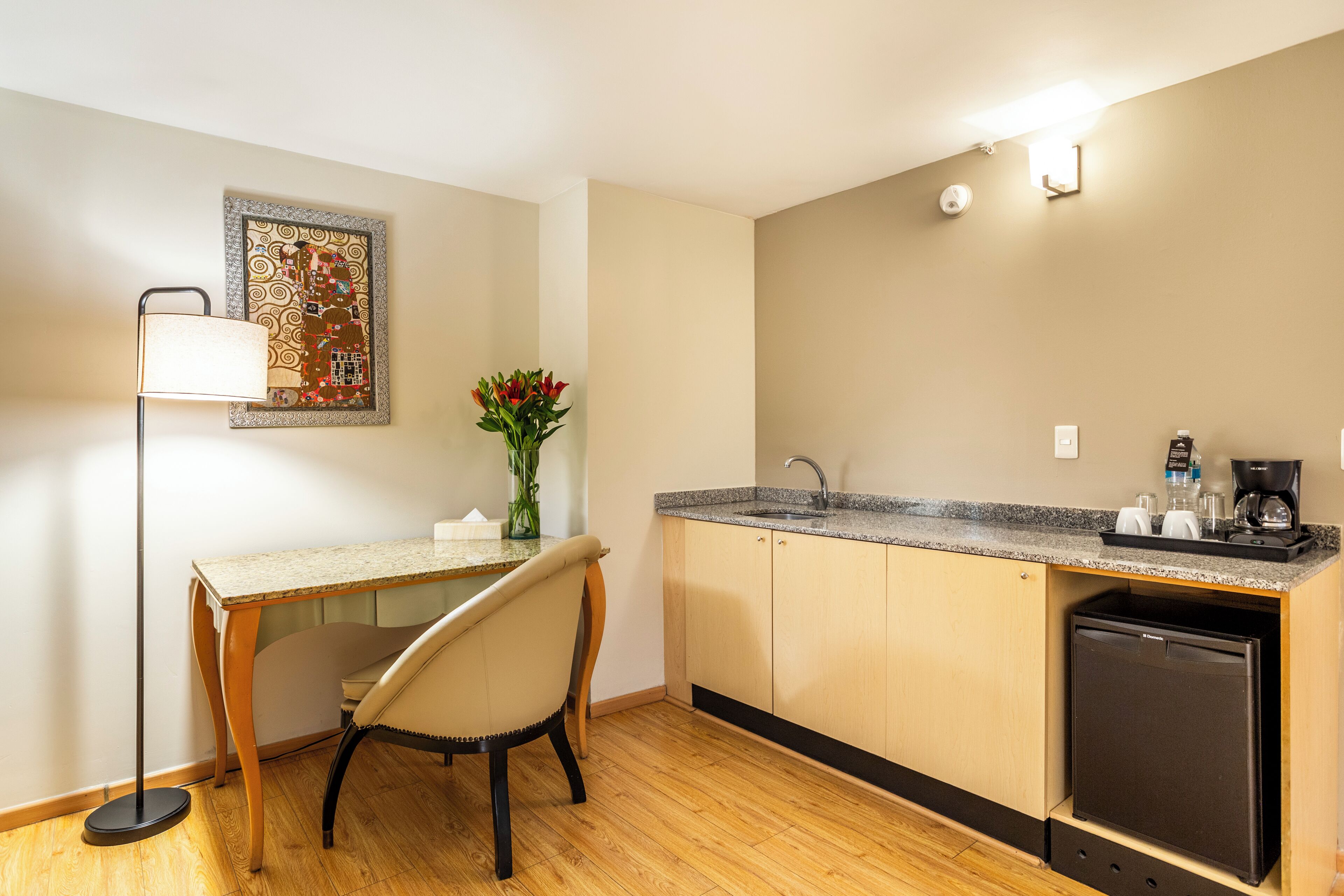 A compact kitchen with a dining area, a small refrigerator, and a wall-mounted light fixture.