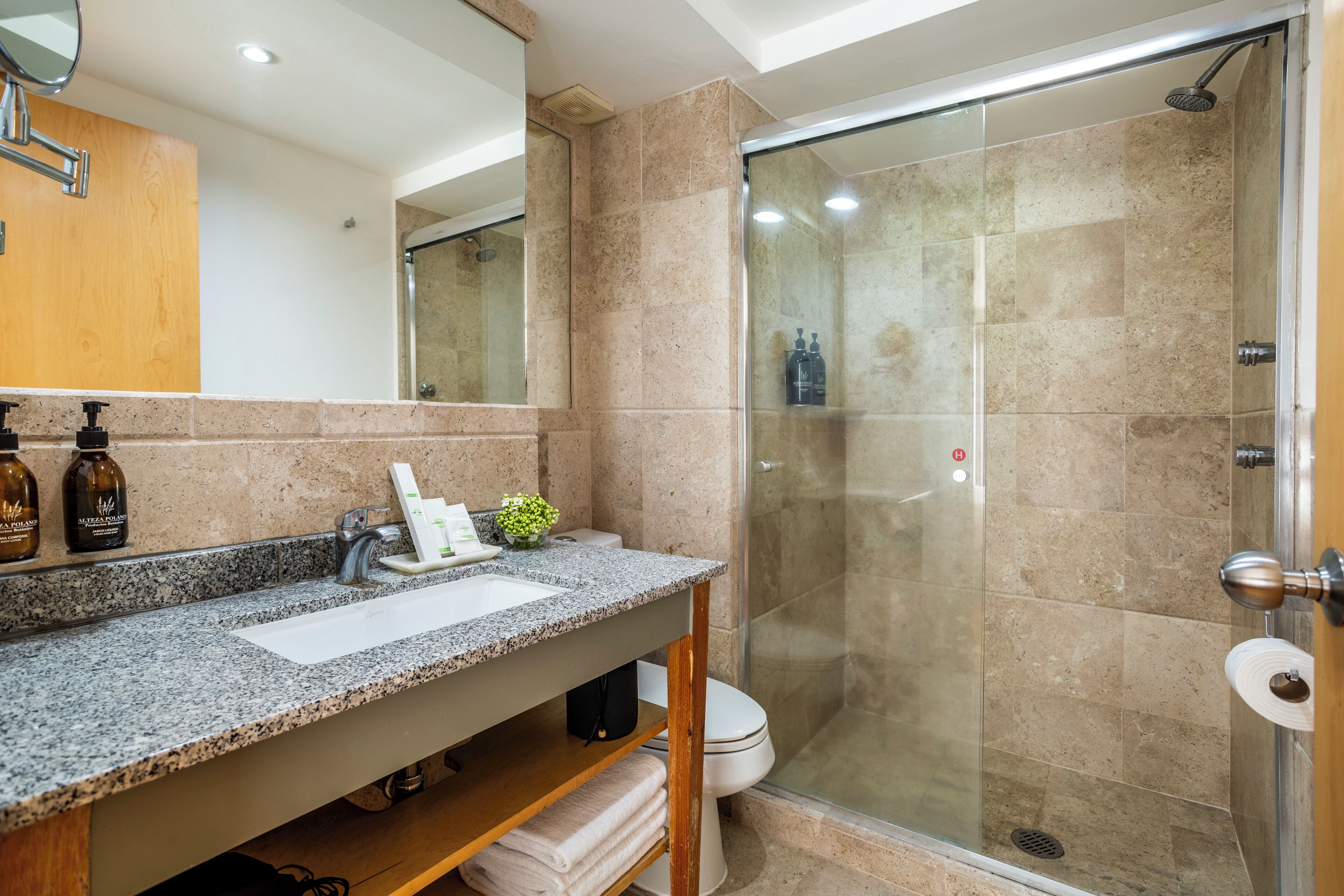 Une salle de bain moderne avec un comptoir en granit, une cabine de douche en verre et un meuble-lavabo en bois.