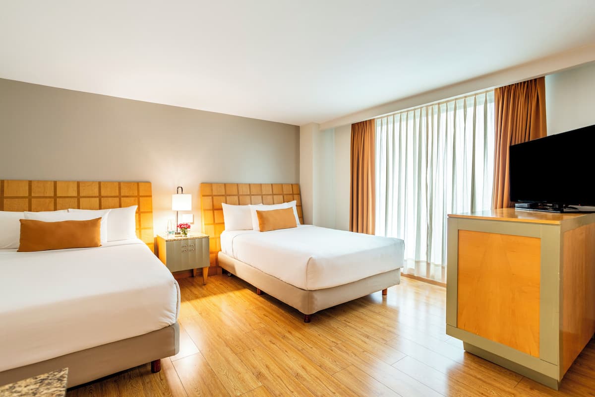 A hotel room with two beds, a TV, a desk, and a window with curtains.