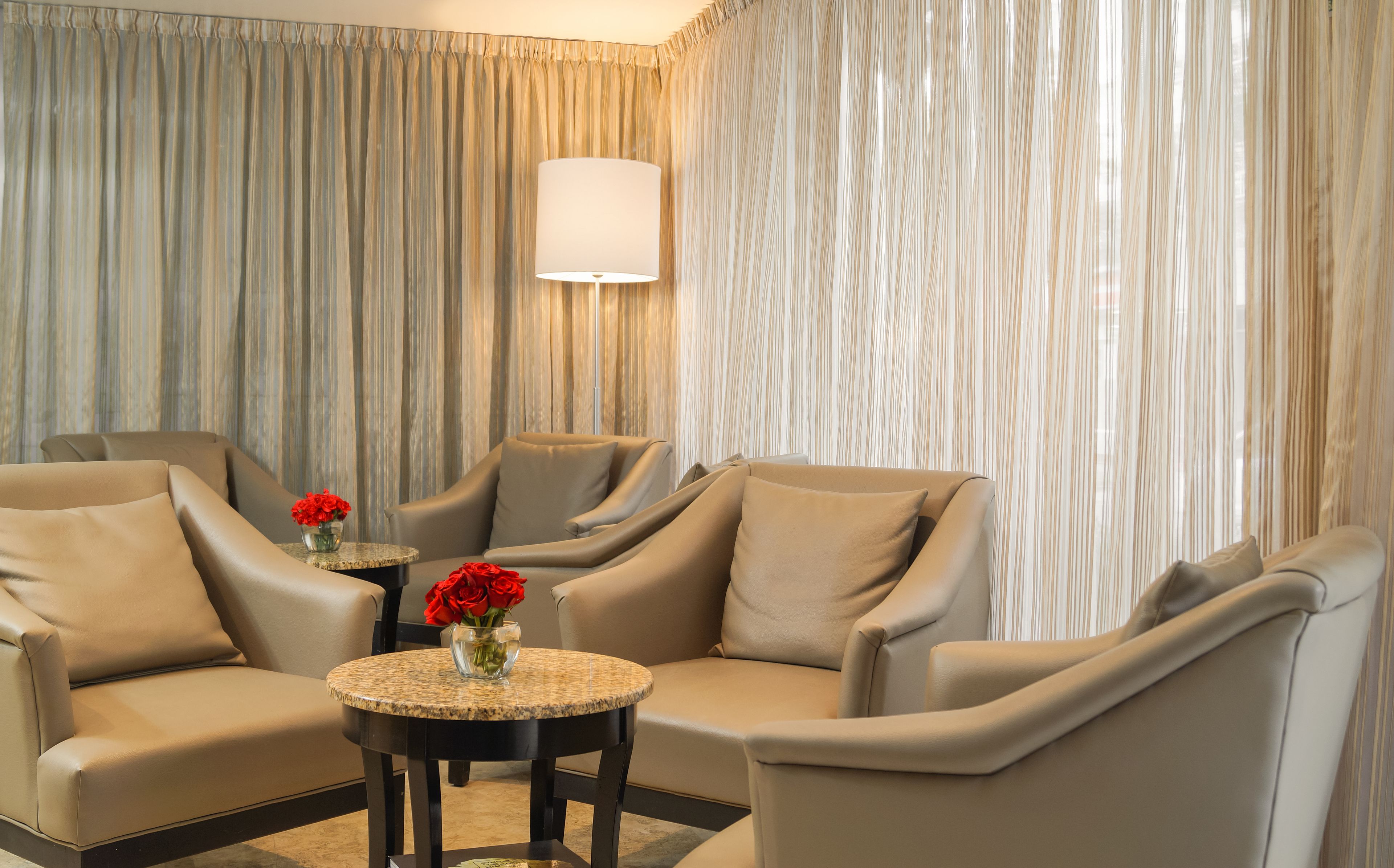 A modern living room with beige leather sofas, a round coffee table, and a vase of red roses.