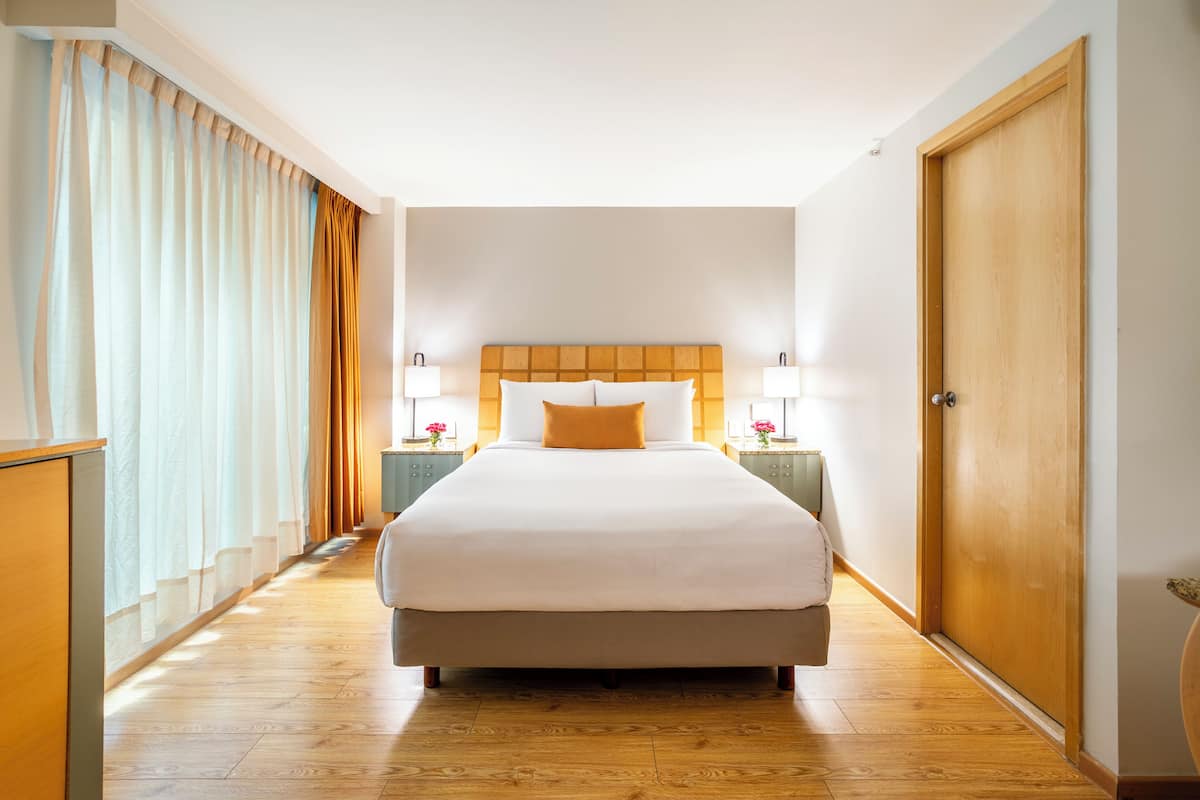 A hotel room with a large bed, wooden floor, a wooden door, and two bedside tables with lamps.