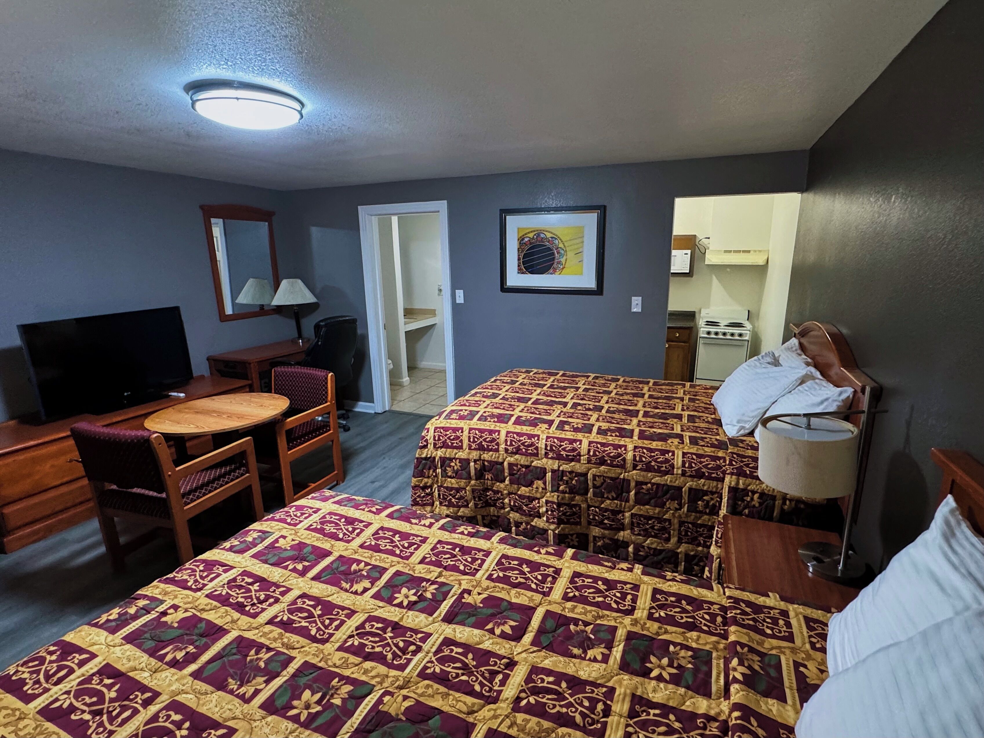 Una camera d'albergo con due letti, una scrivania con televisore, una sedia, una lampada e un bagno.