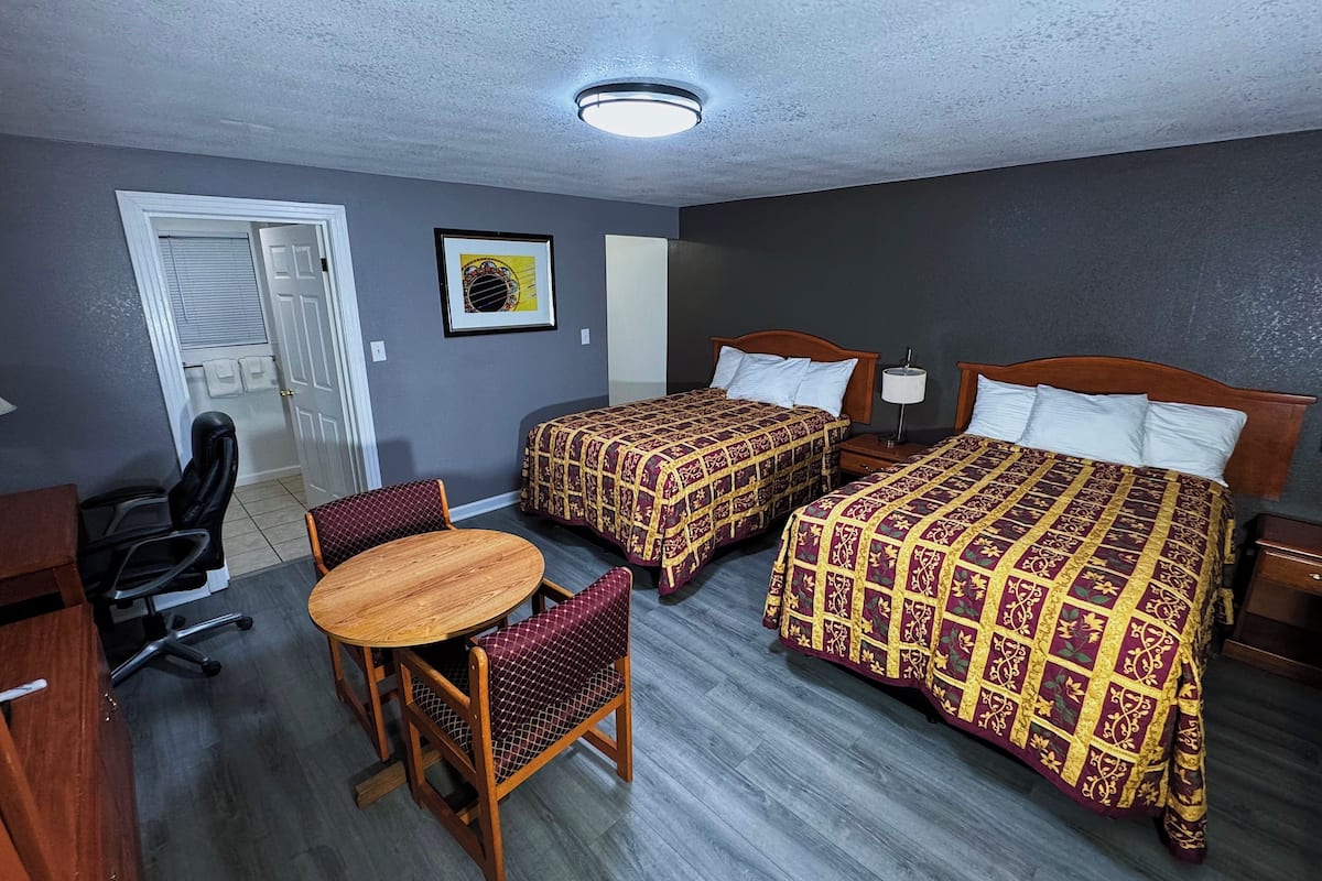 A hotel room with two beds, a desk, a chair, and a small table.