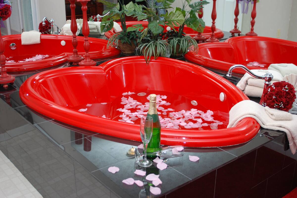 Una bañera roja con pétalos de rosa y una botella de champán.