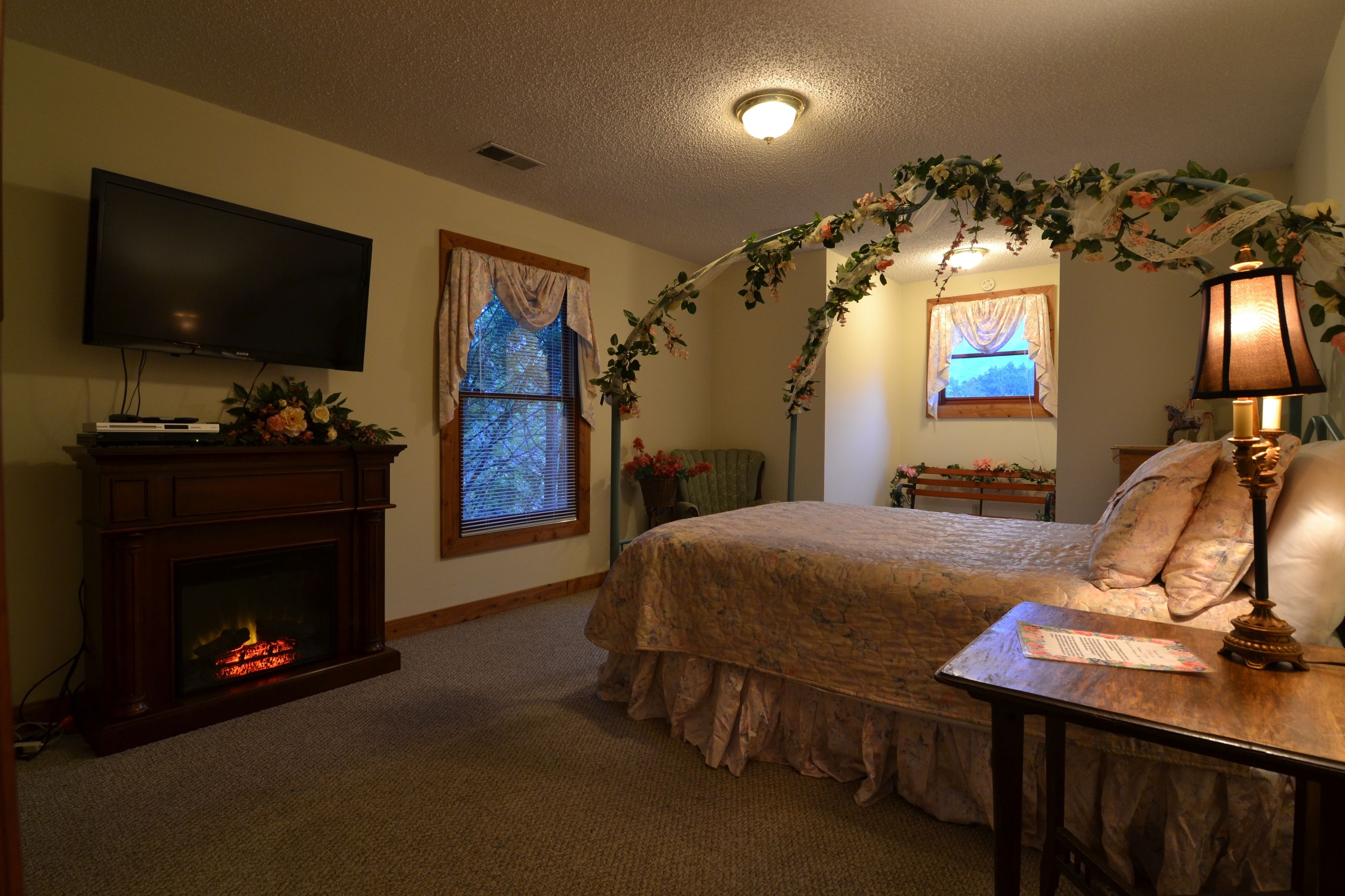 A bedroom with a fireplace, a television, a bed with floral decorations, and a lamp.