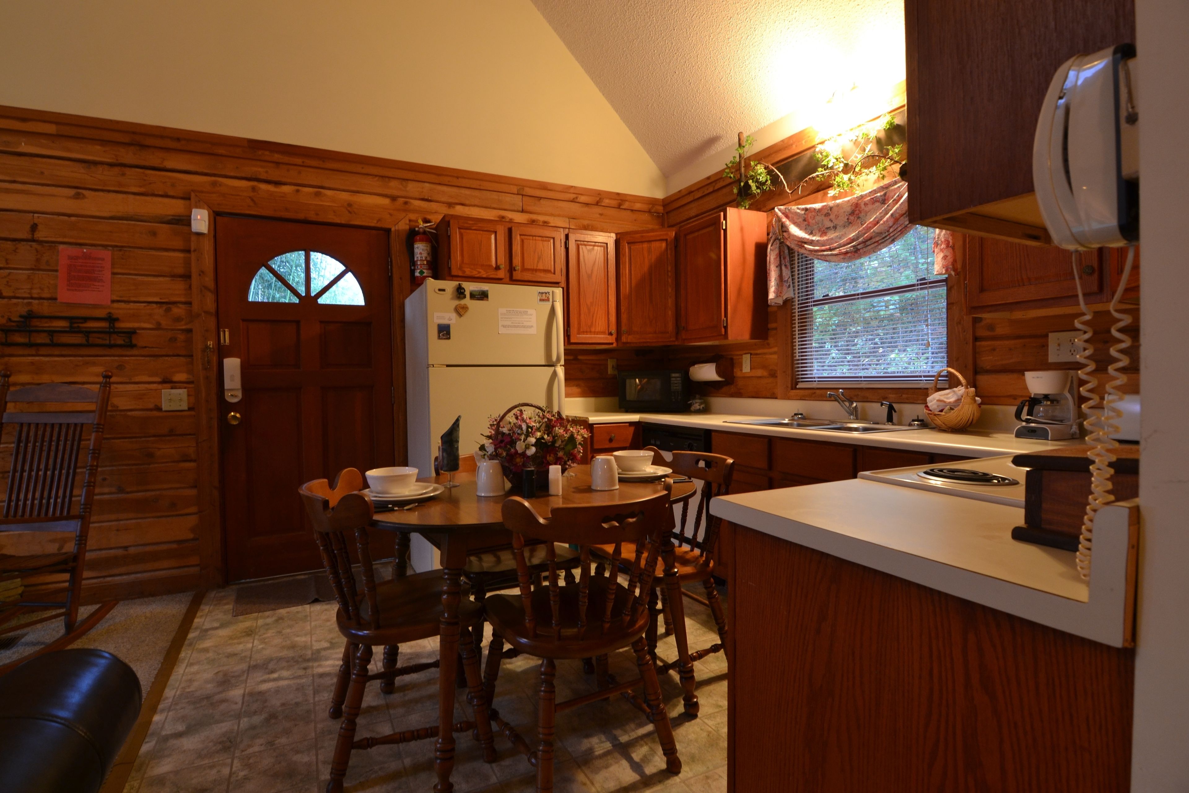 A kitchen with wooden cabinets, a refrigerator, a sink, and a dining area with chairs and a table.