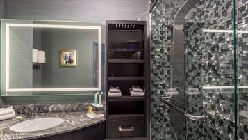 Un baño moderno con un lavabo de mármol, un espejo grande, una televisión integrada y una cabina de ducha de vidrio.