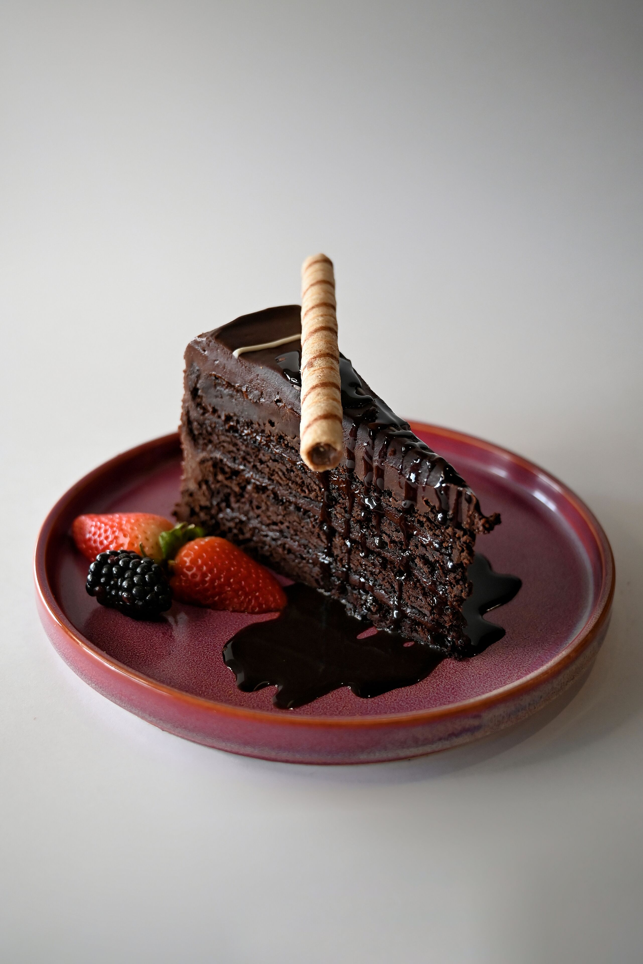 Une part de gâteau au chocolat, servie sur une assiette avec des fraises et nappée d'un coulis de chocolat.