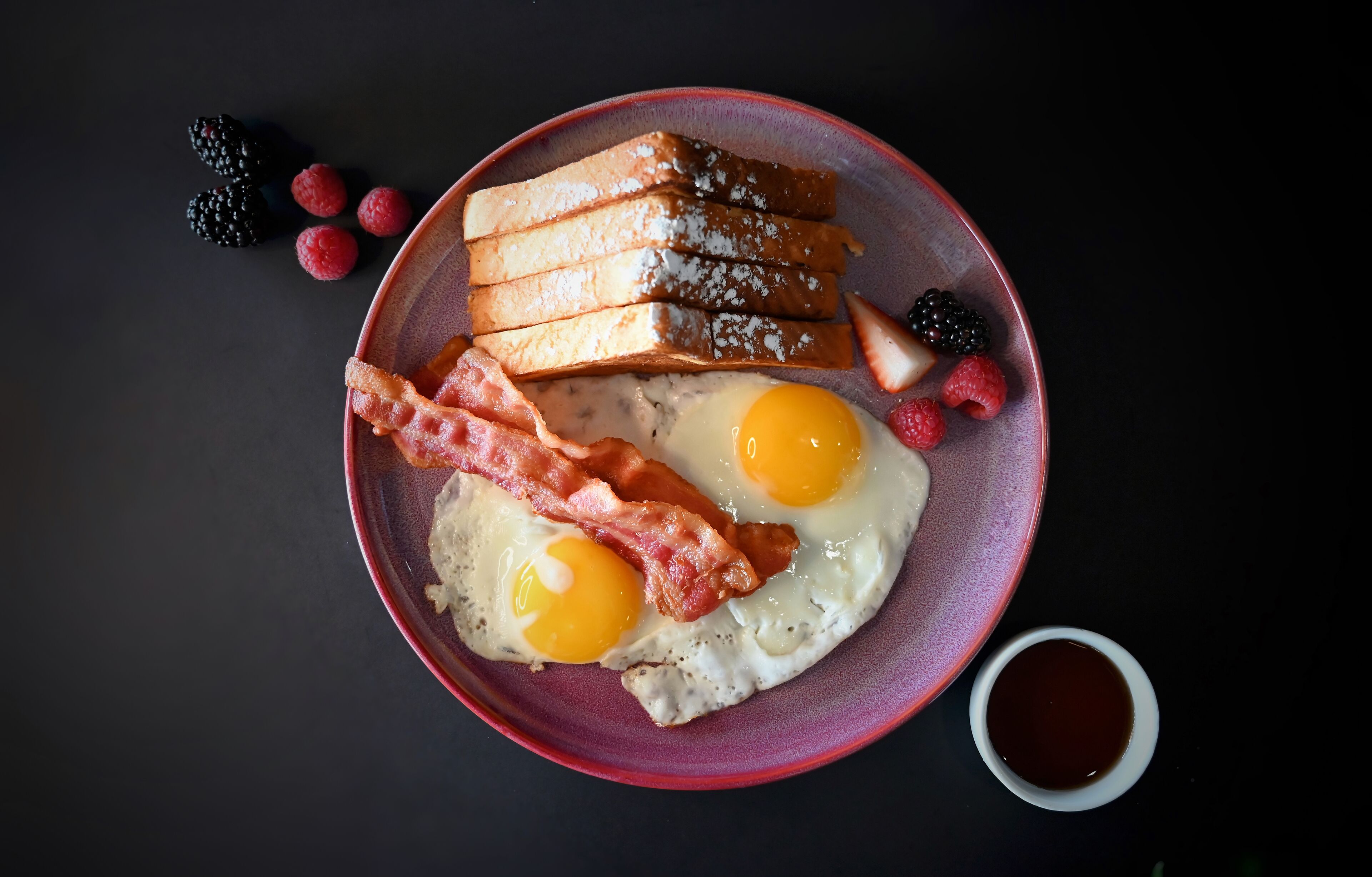 A breakfast plate with eggs, bacon, toast, and berries.