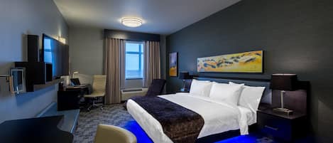 Una habitación de hotel moderna con una cama grande, un escritorio, una silla, un televisor y un cuadro en la pared.