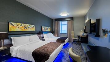 A hotel room with two beds, a desk, a TV, and artwork on the walls.
