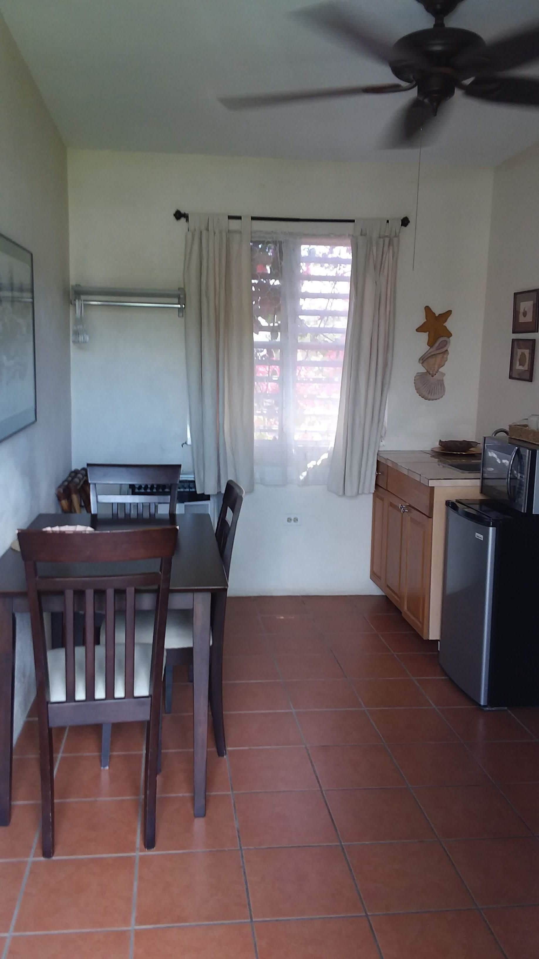 A compact kitchen with a dining area, a ceiling fan, and a window with curtains.