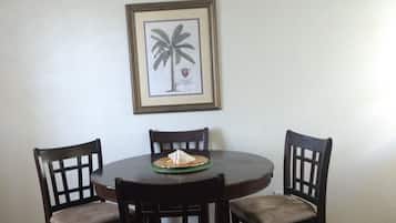 A dining area with a round table, four chairs, a ceiling fan, and a framed picture on the wall.