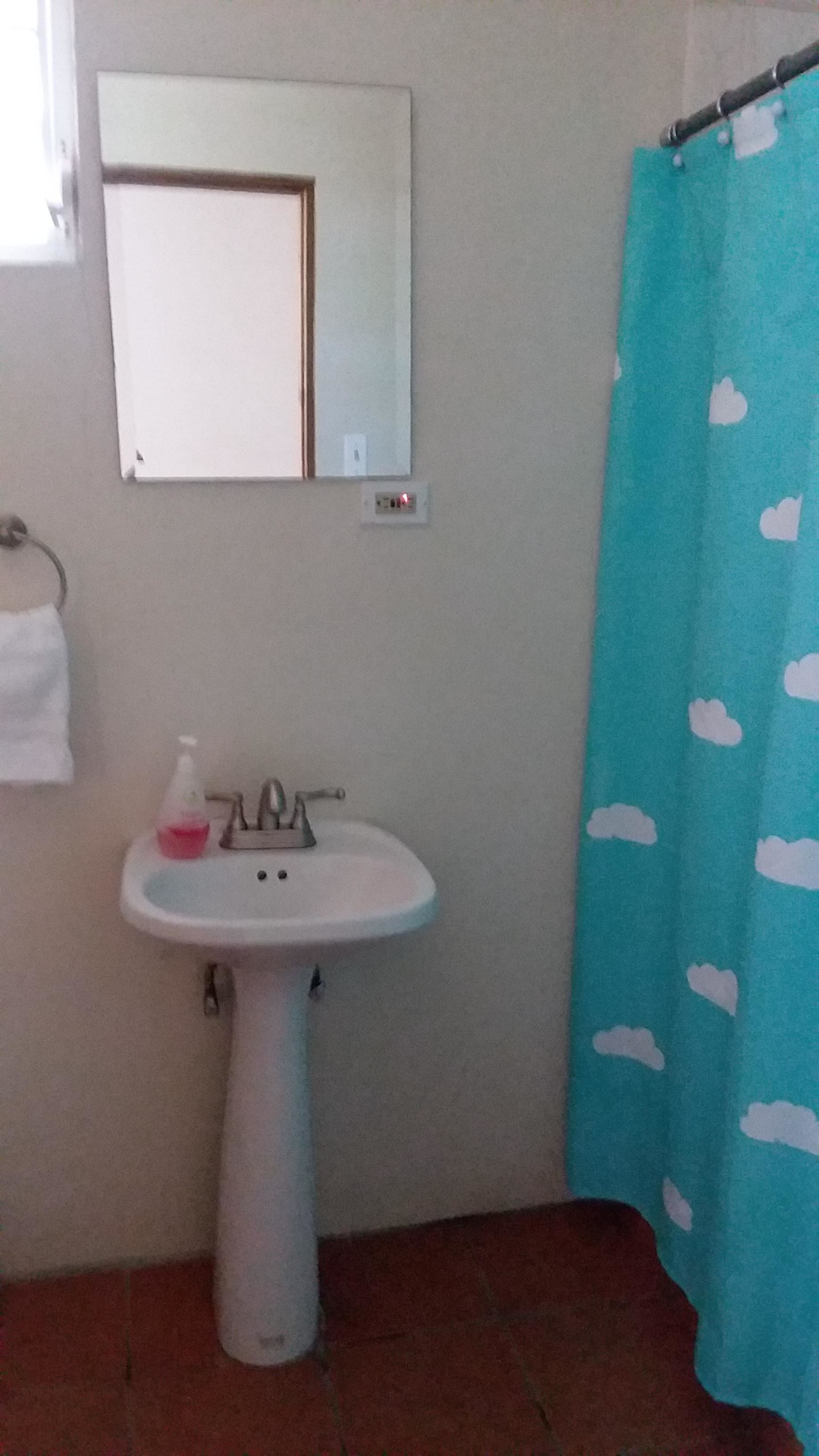 Un bagno con un lavandino bianco, uno specchio sopra e una tenda blu da doccia con motivi a nuvole.