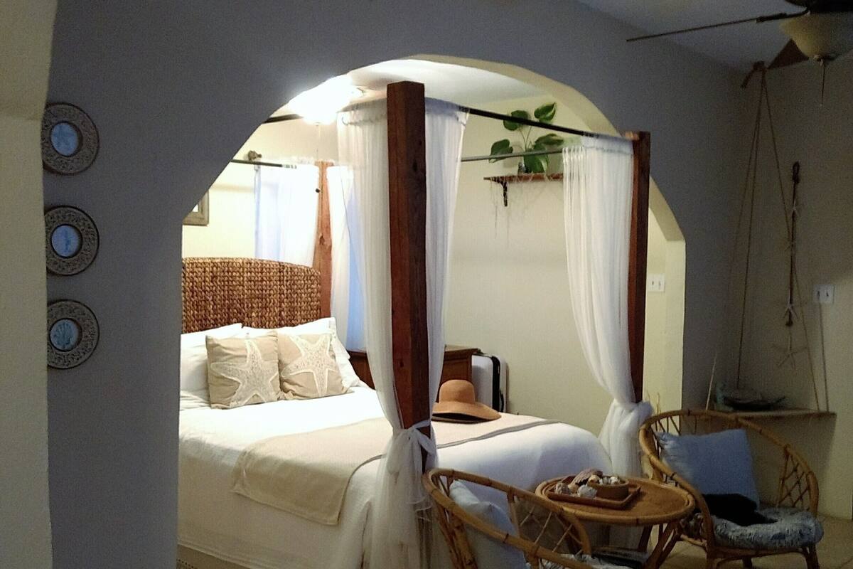 A bedroom with a canopy bed, a small table with chairs, and a ceiling fan.