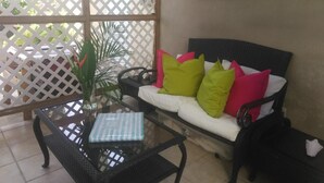A room with a glass-top table, a white sofa with green and pink cushions, a framed picture on the wall, and a lattice door. - Casa de Tortuga (Vieques)