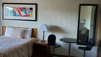 A hotel room with a bed, a desk, two chairs, a lamp, and a large mirror.