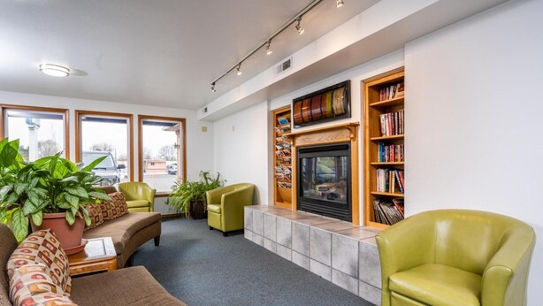 Una sala de estar moderna con chimenea, sillones verdes, un sofá y una estantería.