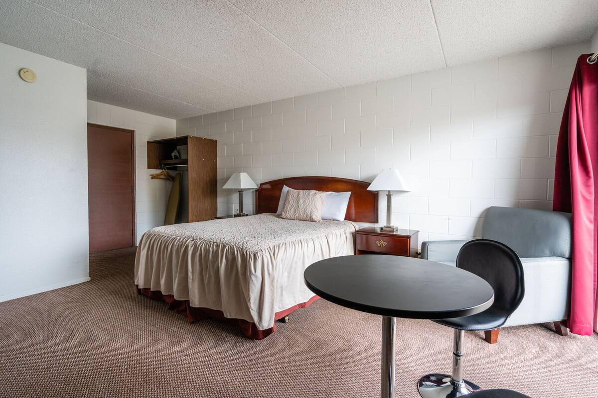 A hotel room with a bed, bedside table, lamp, chair, and a small round table.