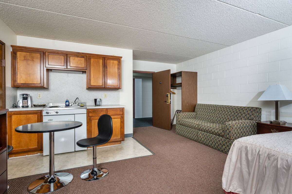 A compact hotel room with a kitchenette, a dining area, a sofa, and a bed.