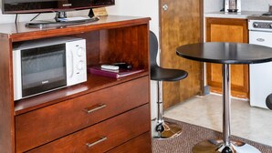 Habitación de hotel compacta con tocador de madera, microondas, televisor Samsung, pequeña mesa de comedor y kitchenette con cafetera.