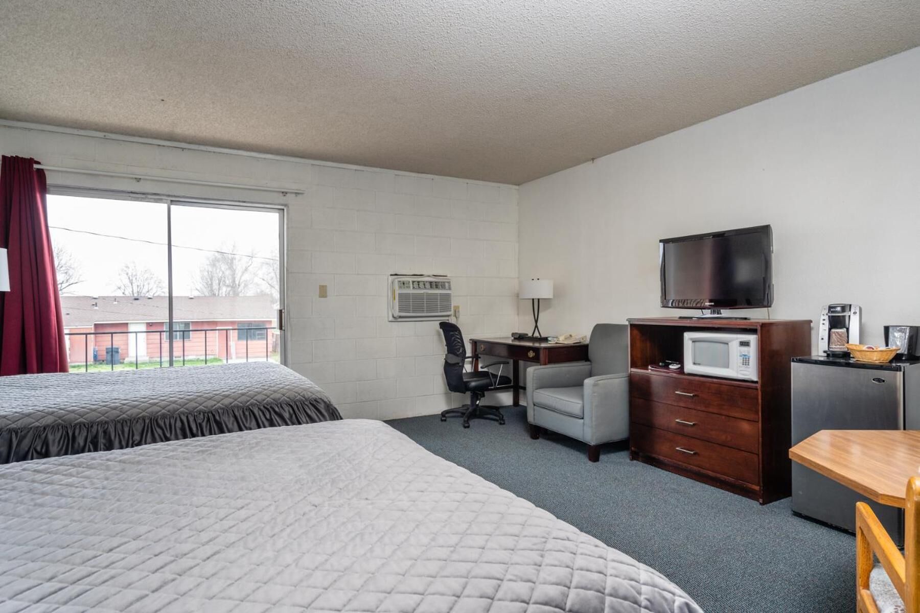 A hotel room with two beds, a desk with a TV, a microwave, and a coffee maker.