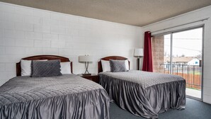 Habitación de hotel con dos camas, paredes de ladrillo blanco, un ventanal con vista a un patio cercado y una cortina roja.