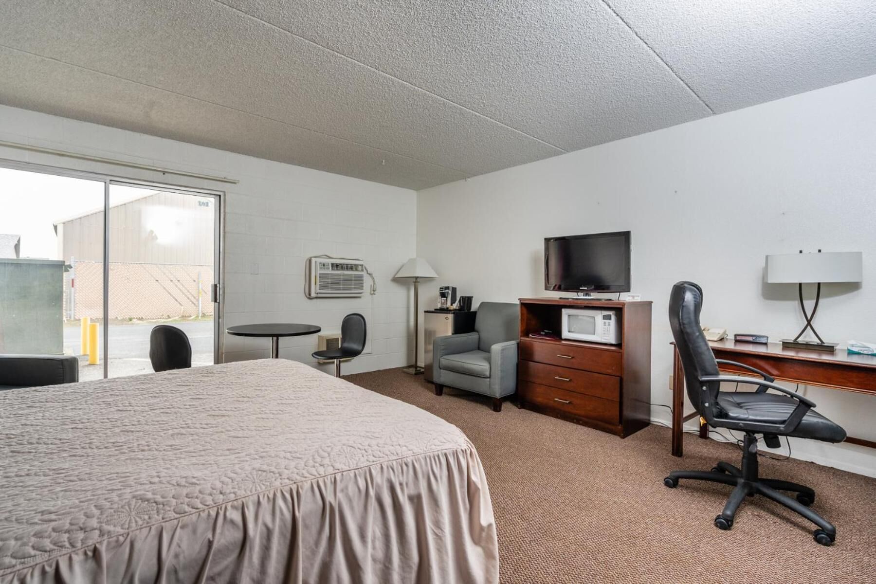 Une chambre d’hôtel comprenant un lit, un bureau avec un ordinateur, une télévision, une chaise, une lampe et une petite table.