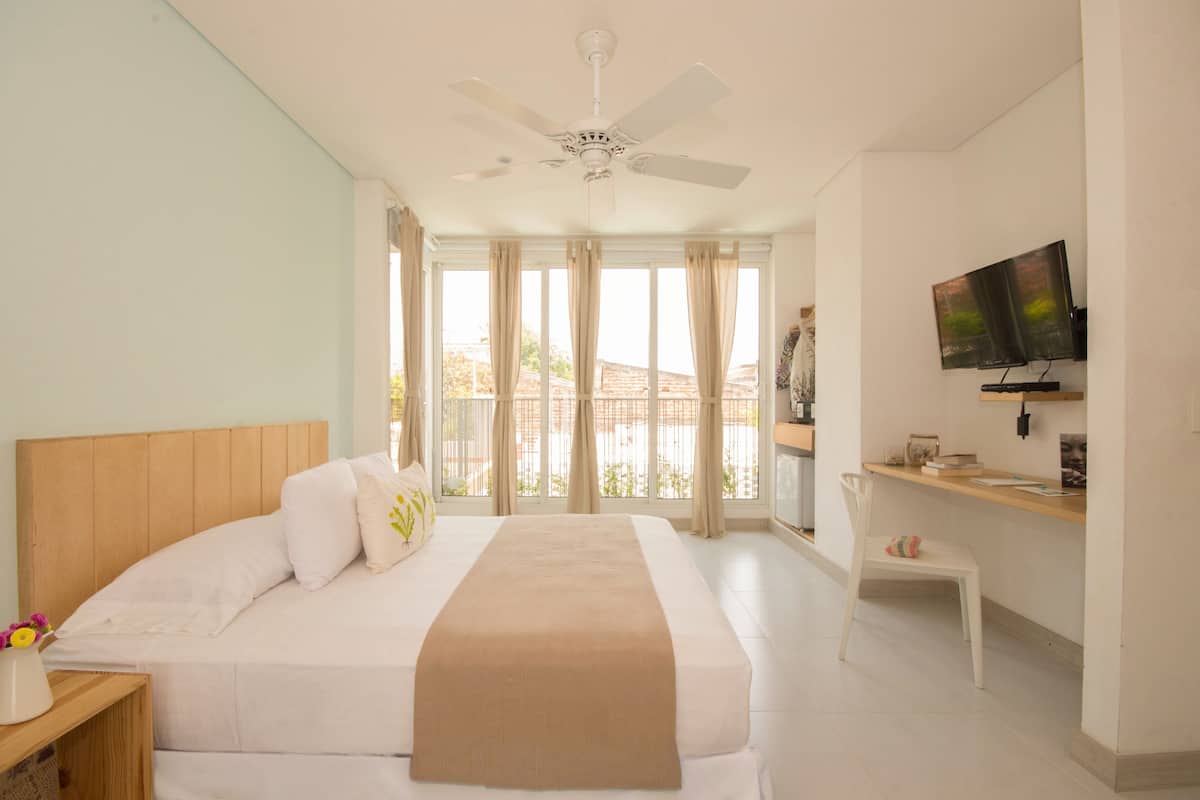 Ein Hotelzimmer mit Bett, Schreibtisch, Sessel, Fernseher und Deckenventilator.