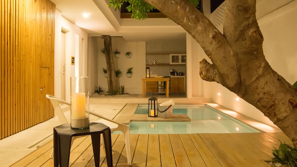 A modern outdoor pool area with a wooden deck, a glass table with a candle, and a stone wall. - La Casa del Patio Hotel Boutique by Xarm Hotels (Santa Marta)