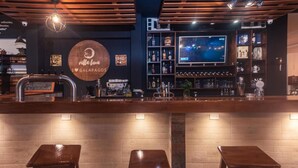 A bar area with a wooden counter, two stools, a television screen, and shelves with bottles. - Galapagos Native (Puerto Ayora)